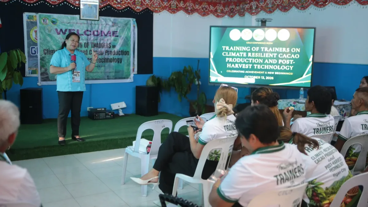 Acting Iligan City Agriculturist Teodosia D. Jaraba speaks into a microphone in front of a digital screen during the culmination of the Training of Trainers on Climate-Resilient Cacao Production and Post-Harvest Technology.
