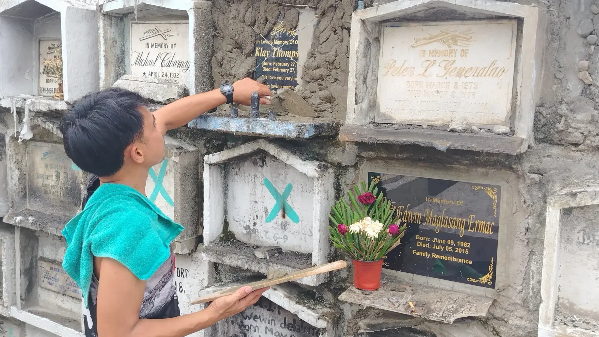 A man applies fresh cement to seal an apartment niche grave at a public cemetery in Iligan City ahead of the annual Undas observance.