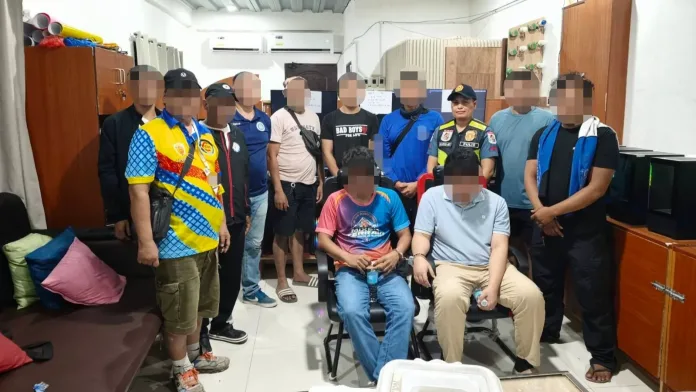 Police officers stand alongside arrested individuals surrounded by confiscated computer hardware following an anti-POGO operation at a business establishment in Barangay Hinaplanon, Iligan City.