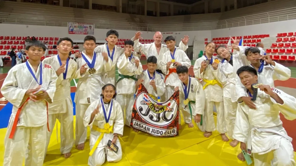 Members of the Jasaan Judo Club wearing white judogi pose enthusiastically on the mat while holding their medals, certificates, and team banner inside the gym in Zamboanga City.