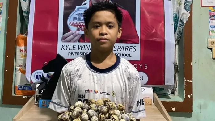 Twelve-year-old chess player Kyle Windylle C. Espares holds a tray of quail eggs in front of his Palarong Pambansa congratulatory poster as he fundraises for the 7th ASEAN+ Individual Chess Championships.