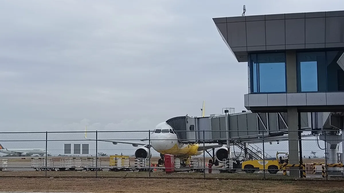An aircraft connected to a boarding bridge at the Laguindingan International Airport tarmac under overcast skies in Misamis Oriental.