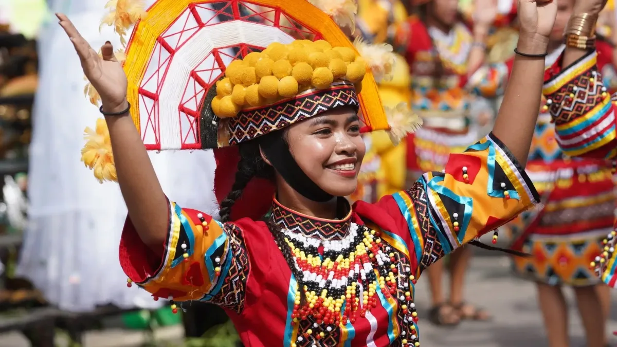 A street dancer wearing a vibrant indigenous-inspired attire decorated with yellow lanzones fruit motifs and a fan-shaped headdress performs during the Lanzones Festival street dance parade in Camiguin.