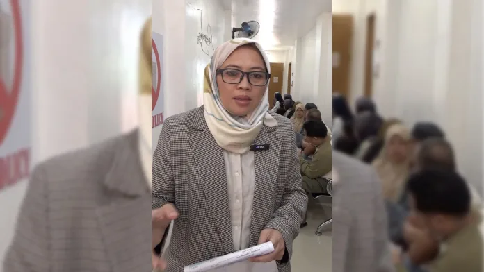 Marawi Compensation Board member Jamaica L. Dimaporo speaks while holding documentation in a hallway, explaining the digital Claims Processing Information System to claimants seeking compensation for the 2017 Marawi siege.