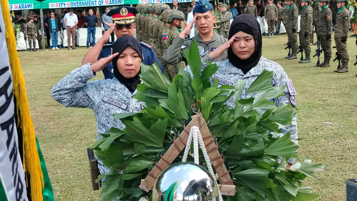 Uniformed military, air force, and police officers in headscarves render hand salutes behind a ceremonial green wreath at the Heroes Wall inside Kampo Ranao during the Marawi Liberation anniversary ceremony.