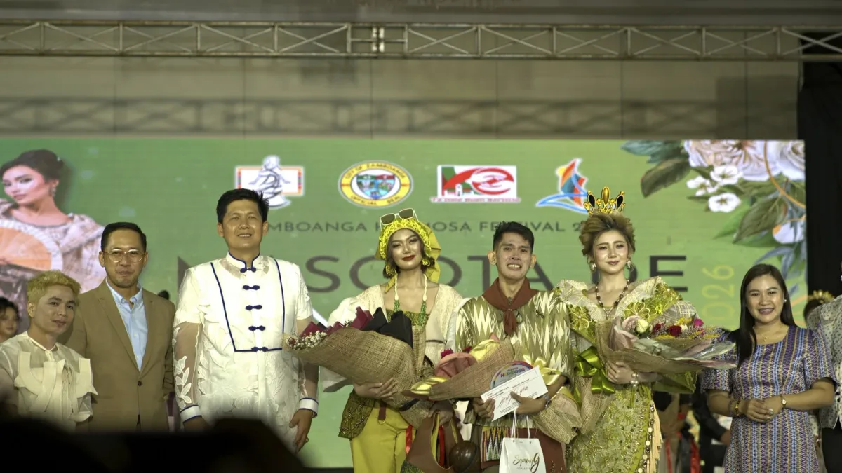 Winning designer Melvin Maverick Uyao holds his certificate and flowers on stage alongside models wearing Mascota de Zamboanga gowns, Zamboanga City Mayor Khymer Olaso, and city officials.