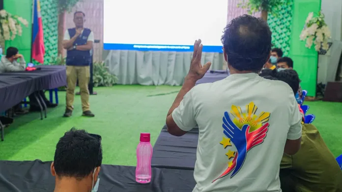 A former rebel wearing a shirt printed with a peace emblem raises a hand to ask a question to Jose Regulus Ortega of OPAPRU during a government assistance orientation at the Misamis Oriental Provincial Capitol Grounds.