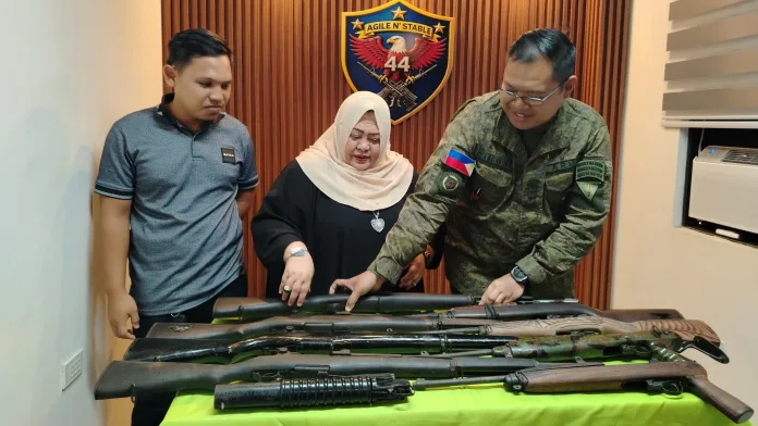 Poona-Piagapo Mayor Ashley “Kaulit” Rakiin and 44th Infantry Battalion Commander Lt. Col. Jeremy Damonsong inspect nine surrendered loose firearms displayed on a table at the 44IB headquarters in Balo-i, Lanao del Norte.