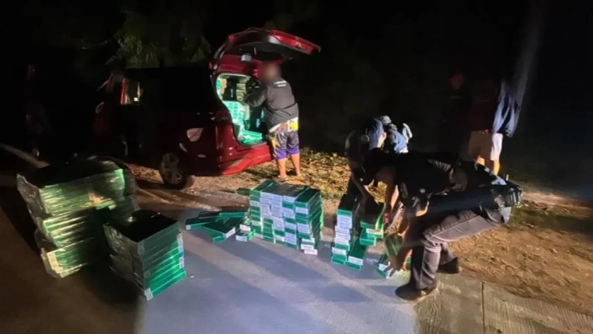 Police officers inspect and stack contraband cigarette reams seized from the open trunk of a red hatchback vehicle during a nighttime anti-smuggling operation in Northern Mindanao.