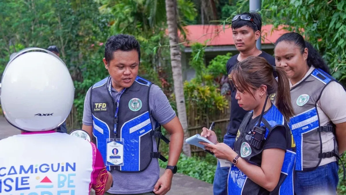 Task Force Disiplina personnel in blue vests inspect a motorcycle rider and issue an Ordinance Violation Receipt during a roadside safety operation in Camiguin.