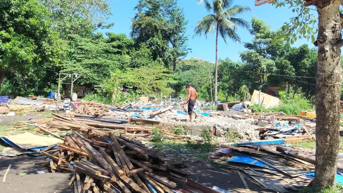 A resident walking through piles of dismantled building materials and wood debris near an outdoor basketball hoop in Upper Puerto, Cagayan de Oro City, following voluntary relocation.
