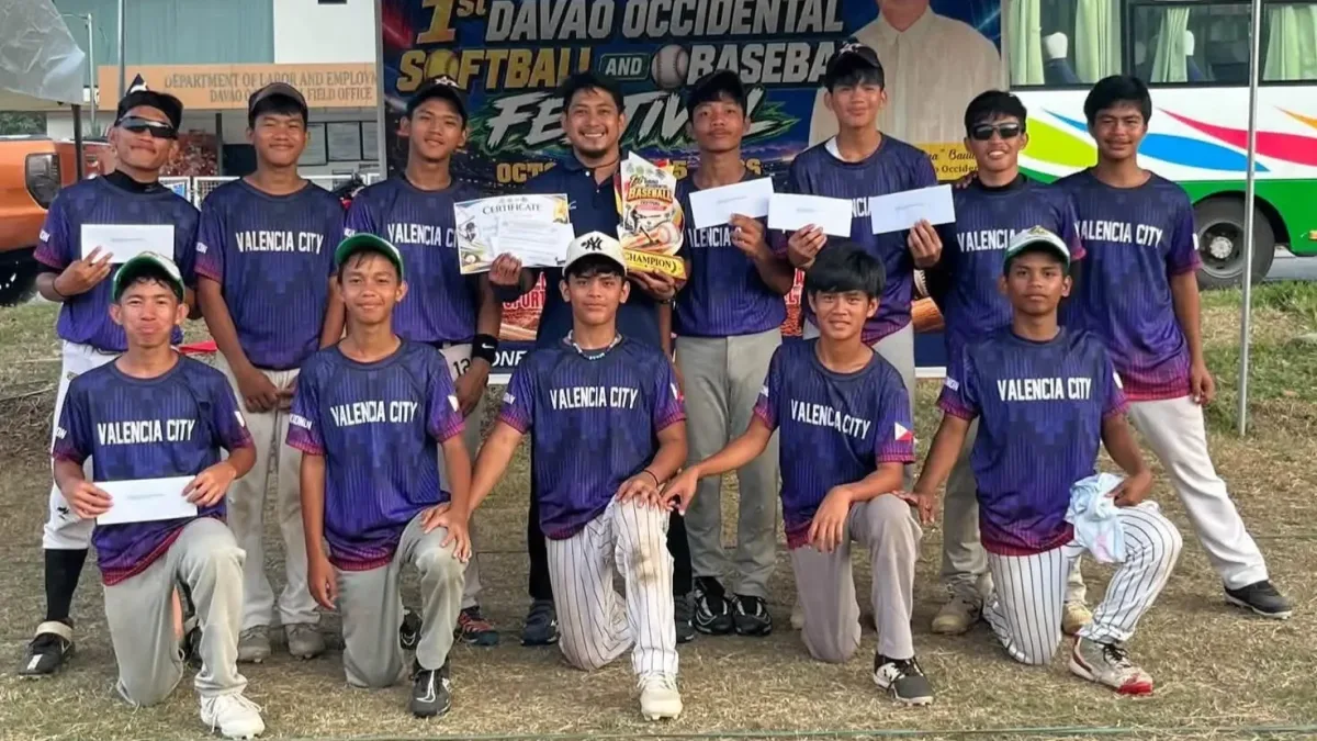 Student-athletes and coaches of the Valencia National High School baseball team, wearing blue jerseys with "Valencia City" branding, display their secondary division championship trophy, certificates, and cash prize envelopes following the 1st Davao Occidental Softball and Baseball Festival.